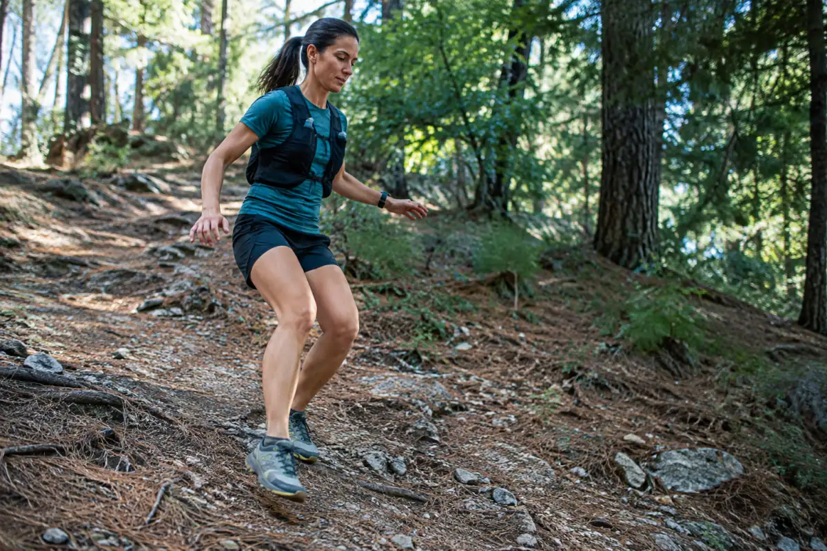 Coureuse de trail en descente sur un sentier forestier, genoux souples et regard porté vers les prochains appuis.