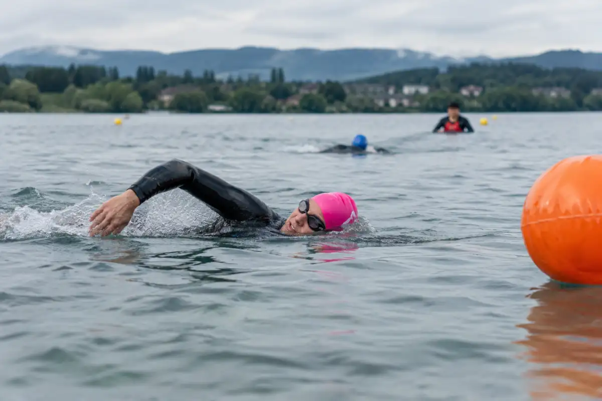 Débutant en combinaison qui relève brièvement la tête pour viser une bouée lors d’un entraînement encadré en eau libre.