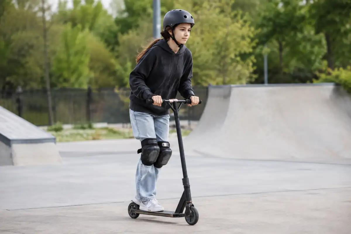 Un pratiquant en trottinette freestyle travaille son équilibre à faible vitesse sur une zone plane et dégagée de skatepark.