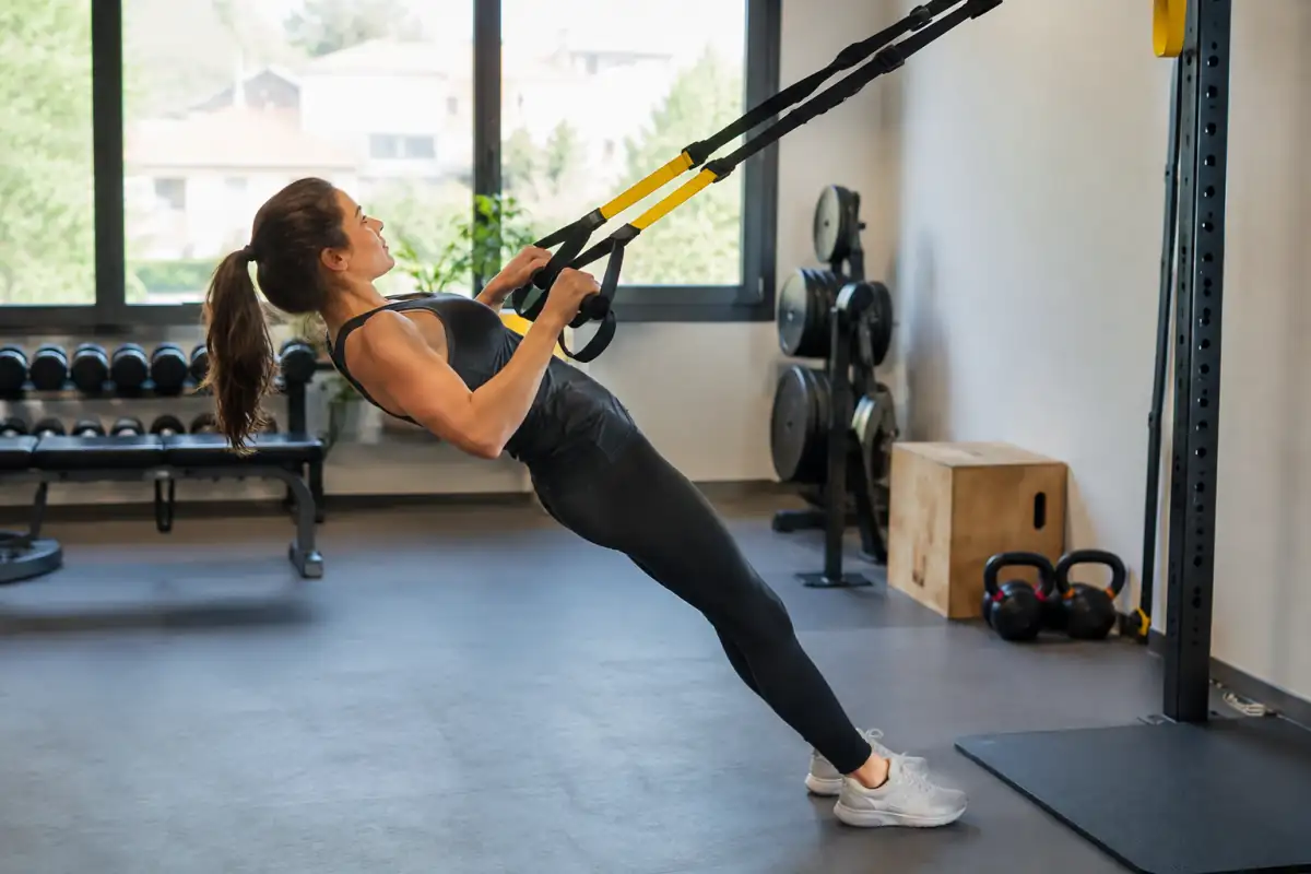 Une sportive réalise un tirage avec des sangles de TRX fixées à un ancrage sécurisé dans une salle de fitness.