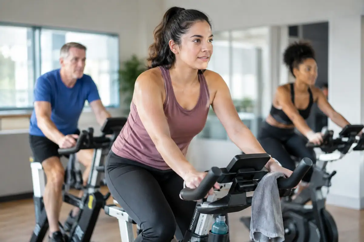 Débutant à vélo indoor pédalant assis à rythme régulier, épaules relâchées et mains posées légèrement sur le guidon.