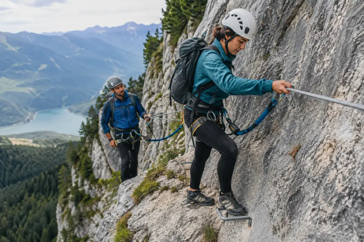 Deux pratiquants équipés progressent sur une via ferrata alpine, longés au câble au-dessus d’une paroi rocheuse.