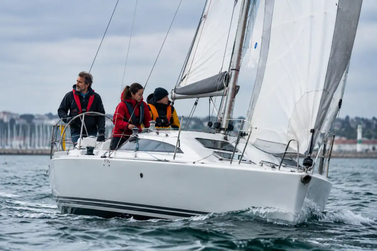 Équipage en gilets de sauvetage réglant les voiles d’un voilier habitable lors d’une sortie côtière.