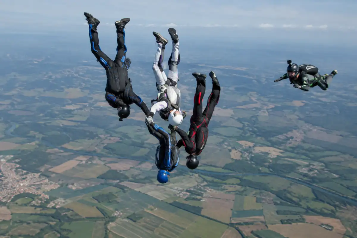 Quatre parachutistes en formation tête en bas pratiquent le vol relatif vertical au-dessus d’une zone de saut.