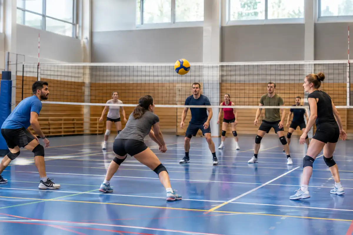 Une réception de service en volley-ball en salle, avec les joueurs répartis sur le terrain autour du filet et des lignes visibles.
