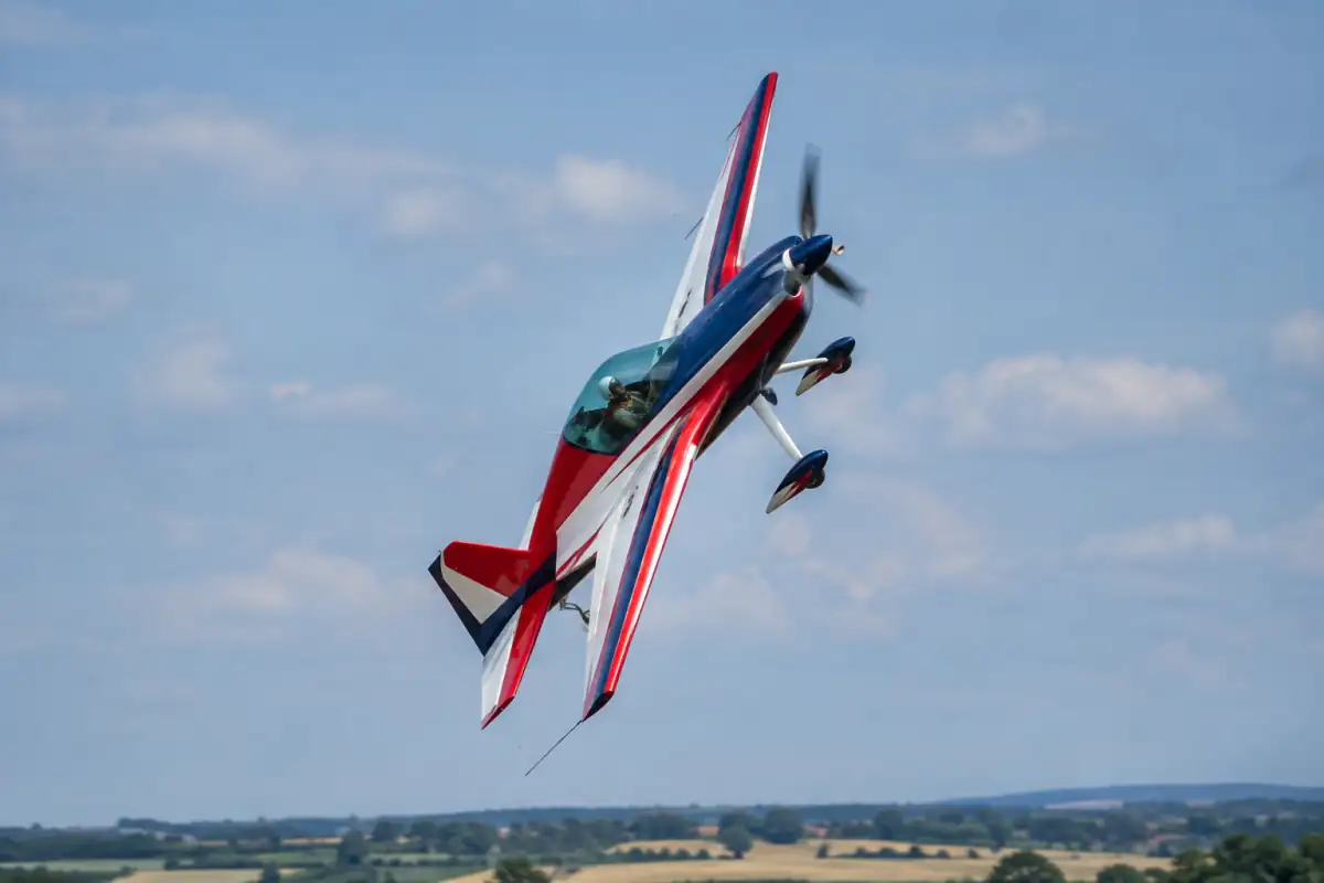 Avion de voltige en plein tonneau au-dessus d’un aérodrome français, piloté avec casque et harnais.