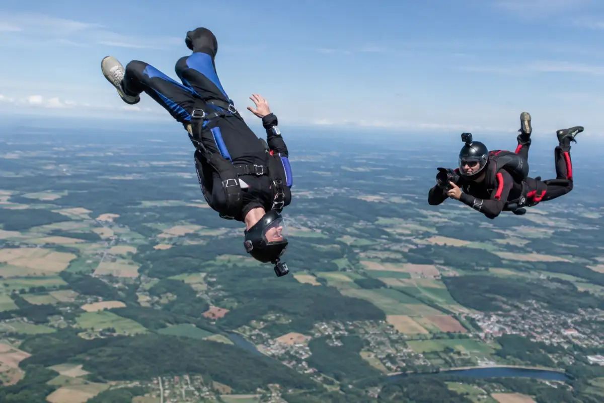 Voltige parachutiste : un pratiquant en combinaison effectue une rotation en chute libre, filmé par un parachutiste caméra.