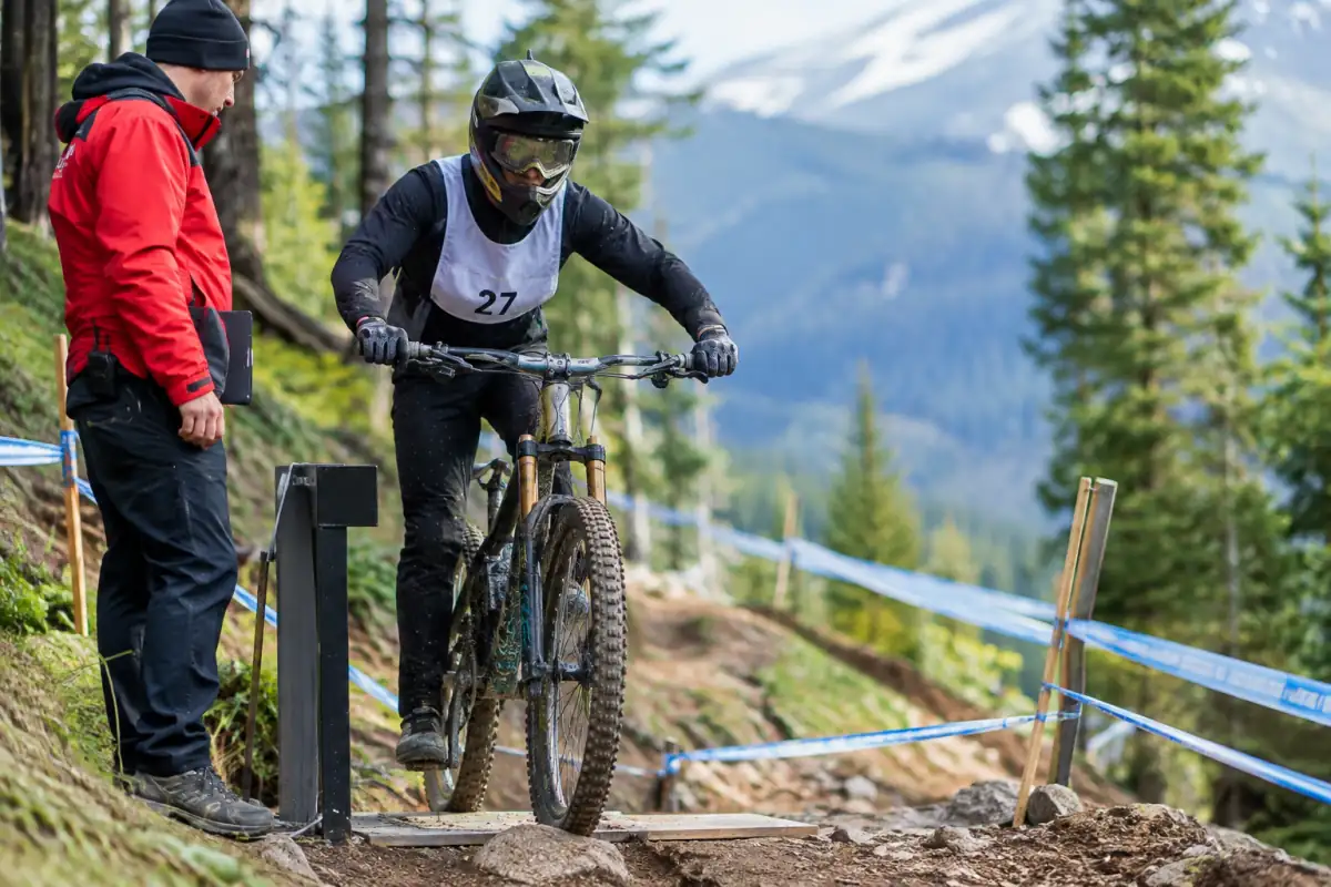 Pilote de VTT de descente en casque intégral attendant le départ individuel près du balisage et du dispositif de chronométrage.