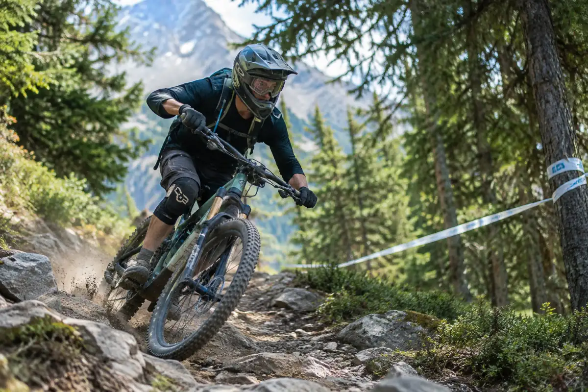 Pilote en casque intégral négociant un virage rocheux sur une spéciale de VTT enduro dans une forêt alpine.