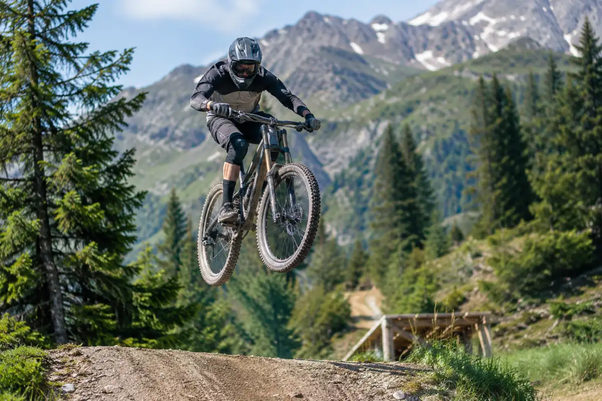 Pilote de VTT freeride en casque intégral franchissant un saut aménagé sur une piste de montagne.