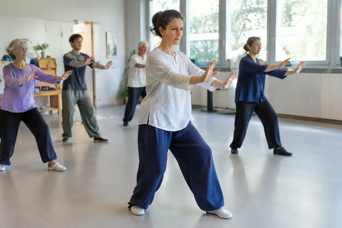 Une pratiquante exécute un mouvement lent de Yi Jin Jing dans une salle, tandis qu’un petit groupe suit la séance.