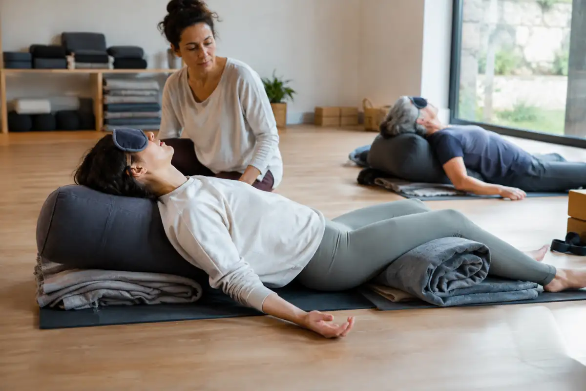 Séance de yoga restauratif : une pratiquante repose le dos sur un bolster, soutenue par des couvertures dans une salle calme.