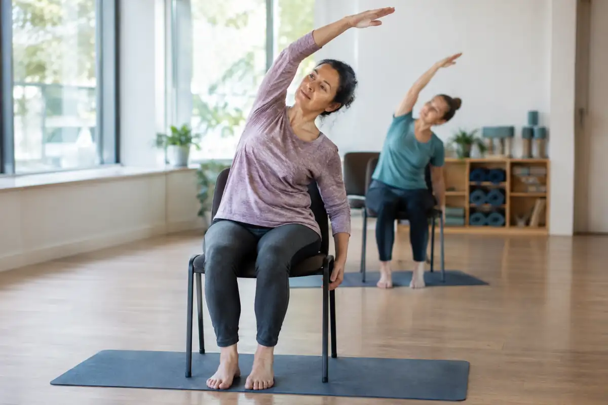 Une pratiquante réalise une inclinaison latérale assise sur une chaise stable pendant un cours de yoga sur chaise.