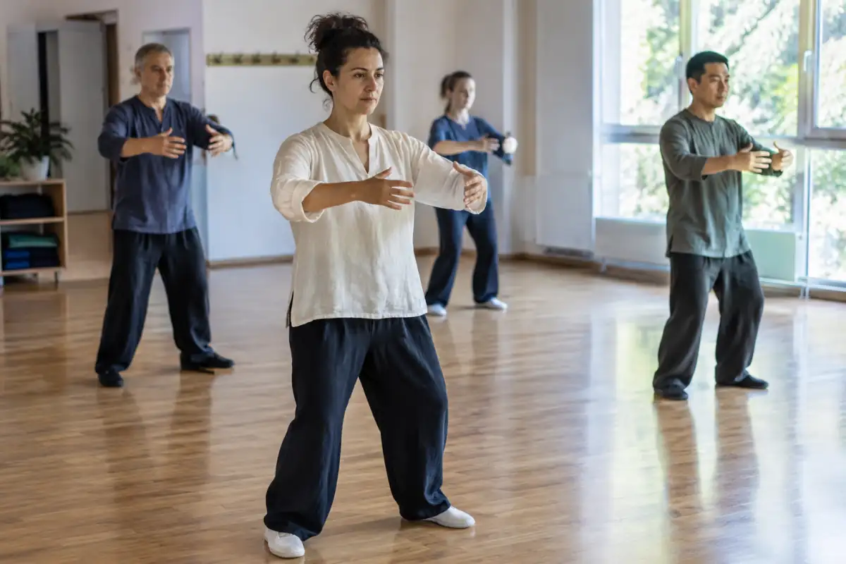 Une pratiquante tient la posture du zhan zhuang, bras arrondis devant le buste et genoux souples, dans une salle de qi gong.